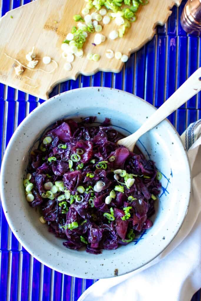 German sweet and sour braised cabbage recipe in a bowl on a blue table. 