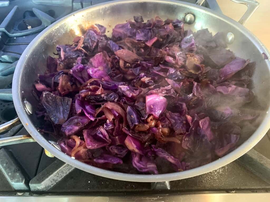 Cabbage cooking in a large frying pan on the stove. 