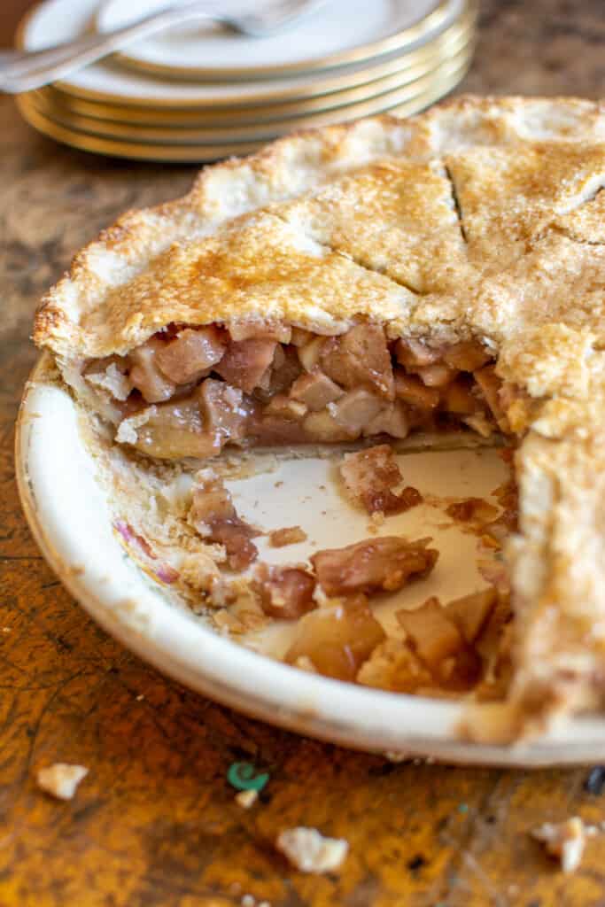 A close up of an apple pie in a pie plate with two pieces missing from the pie and the inside of the pie showing. 