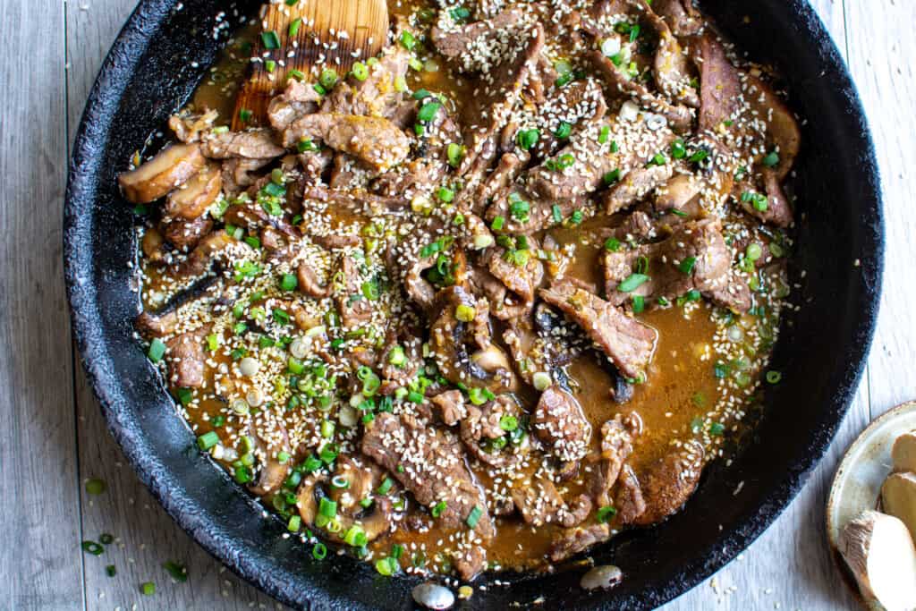 A black frying pan sitting on a gray table topped with sliced green onions and scallions with a wood spoon sticking in.