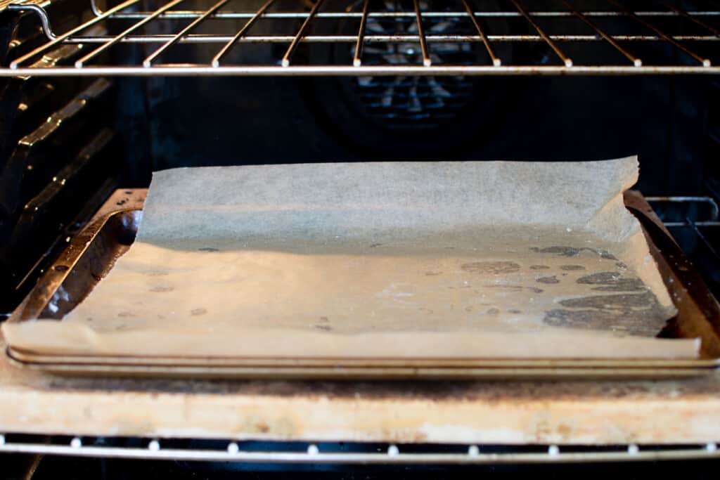 A baking sheet covered with parchment paper sitting on a baking stone on a rack in the oven. 