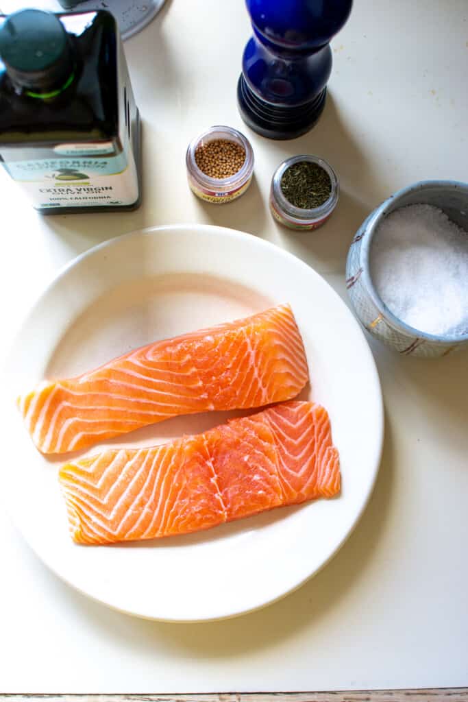 All the ingredients to make the best salmon recipe including salmon, olive oil, dill, mustard seed, salt, and pepper. 