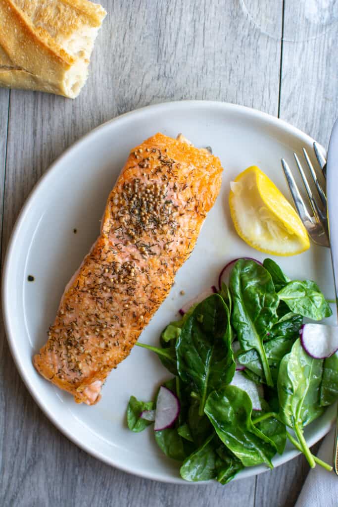 A plate of salmon with a salad on the plate and a lemon wedge that has been squeezed next to it. 