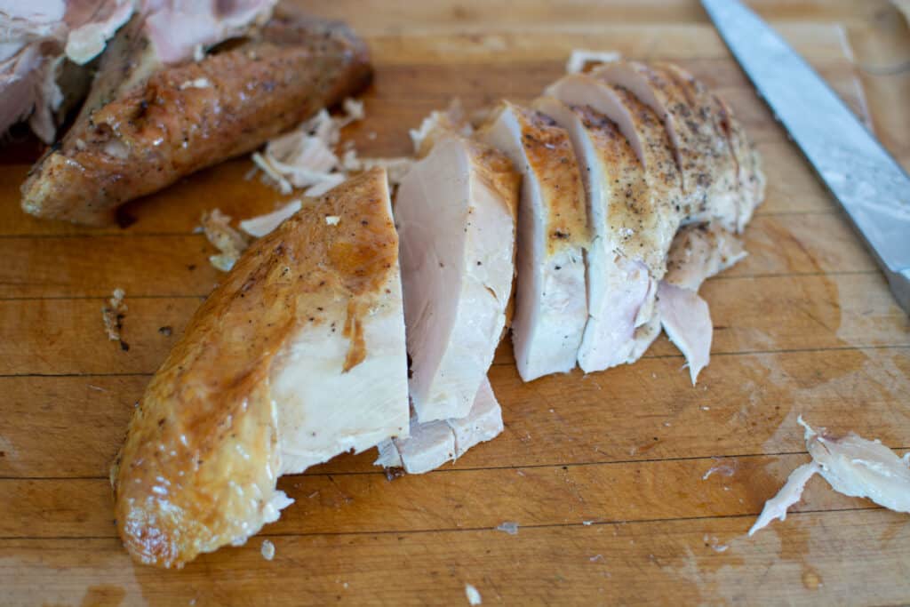 A turkey breast that has been roasted and removed from the turkey being cut into slices on a cutting board. 