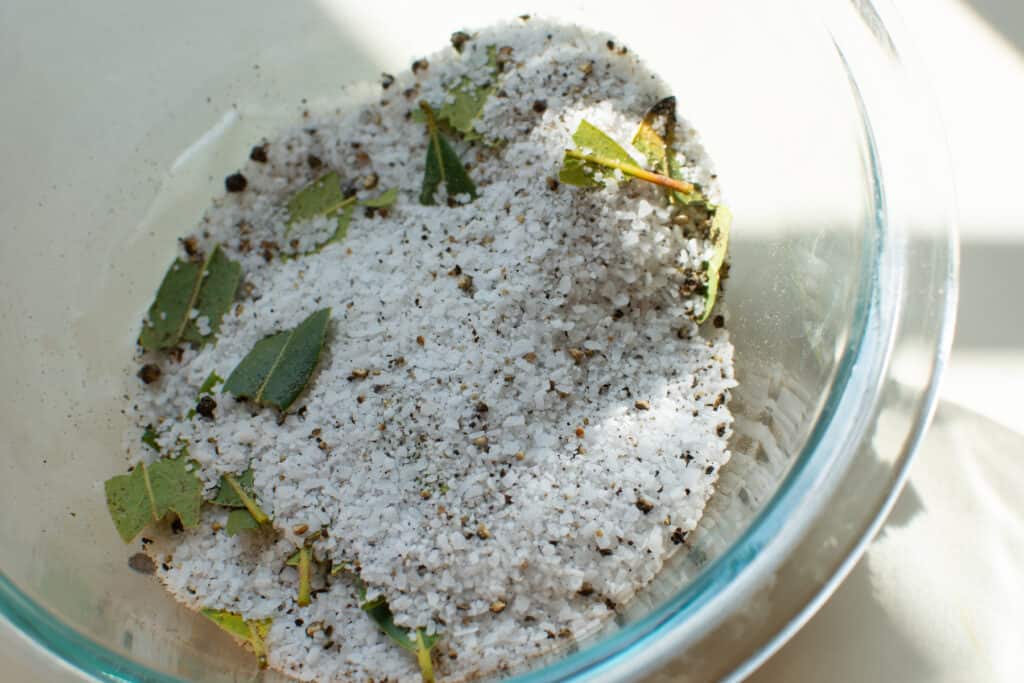 The salt rub for the brine for the turkey in a glass bowl. The rub contains kosher salt, crushed bay leaves and pepper. 