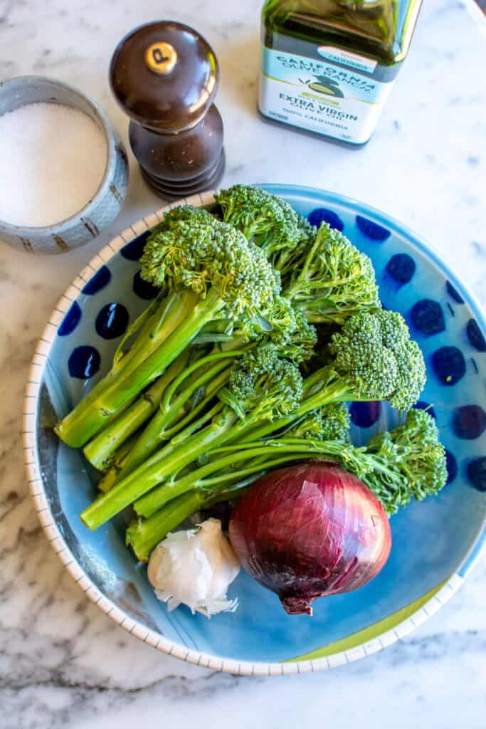 All the ingredients you need to make broccolini including broccolini, red onion, garlic, olive oil, salt, and pepper. 