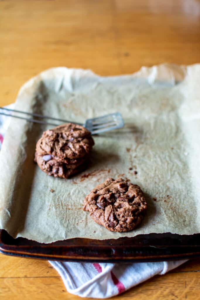 Three cocoa cookies on a baking sheet next to a small spatula.