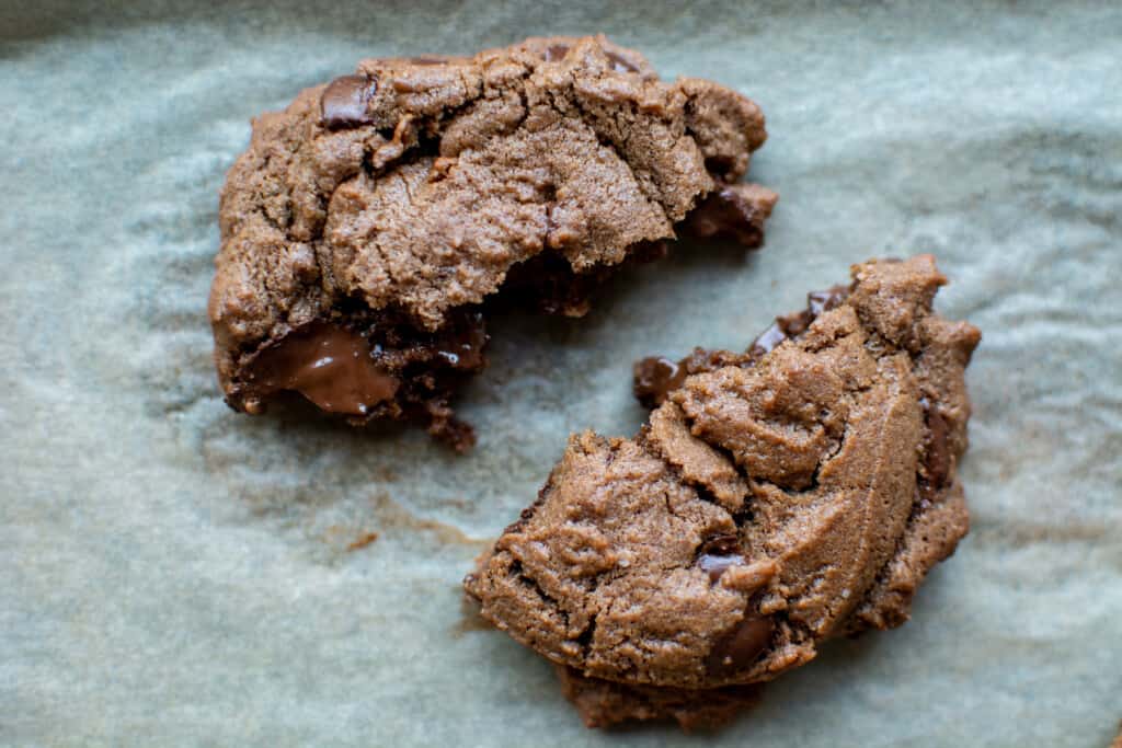 A cocoa cookie with chocolate chips freshly baked and pulled apart so you can see the melted chocolate chips. 