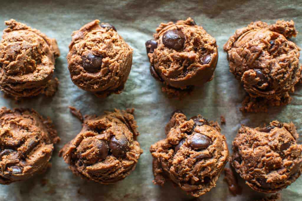 Scoops of chocolate cookie dough on a parchment-lined baking sheet. 