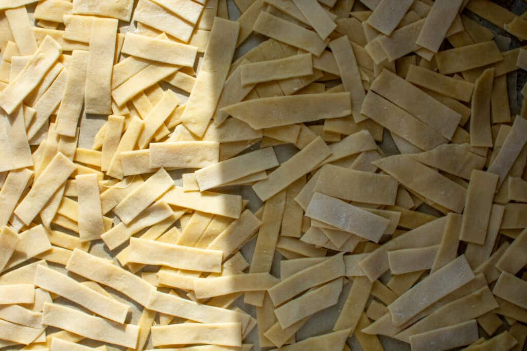 Strips of egg noodles sitting on a parchment-lined baking sheet. 