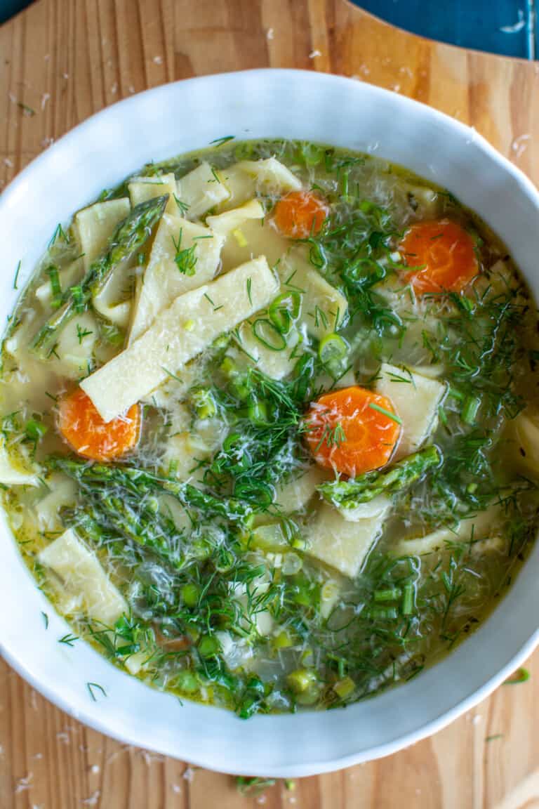 A white bowl filled with egg noodle soup on a wood cutting board.