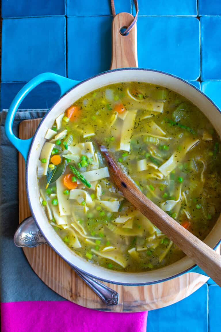A big pot of egg noodle soup sitting on a wood cutting board.
