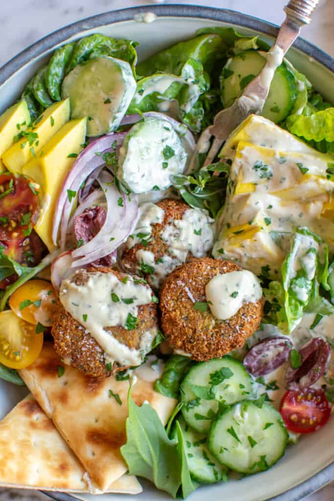 A big bowl of falafel salad with falafel and pita and more.