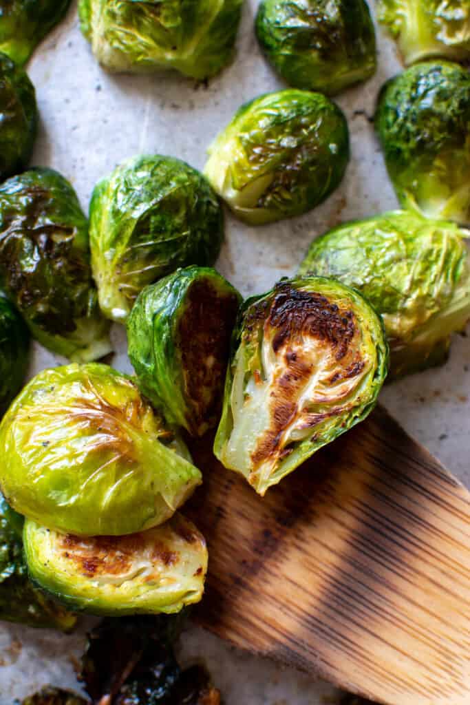 A close up of roasted Brussel sprouts on a baking sheet with a wood spatula lifting a few of them up. 
