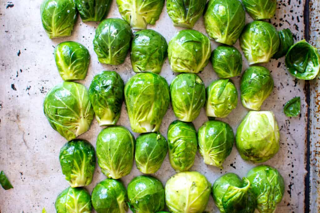 Rows of Brussels sprouts cut in half and lined up on a baking sheet cut side down. 