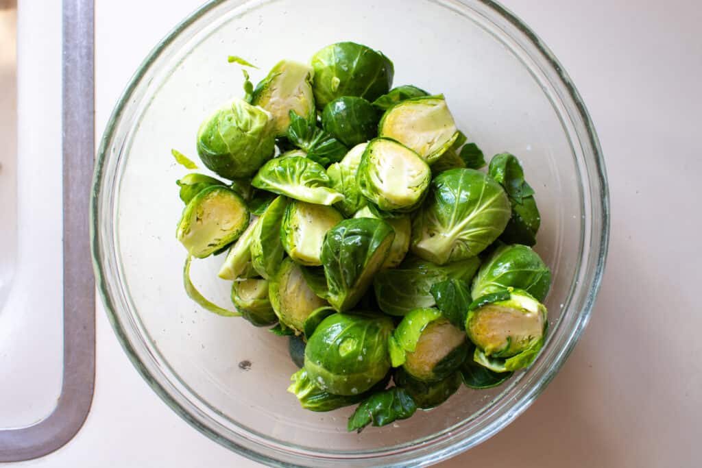 A glass bowl filled with Brussels sprouts cut in half and tossed with olive oil and salt and pepper. 