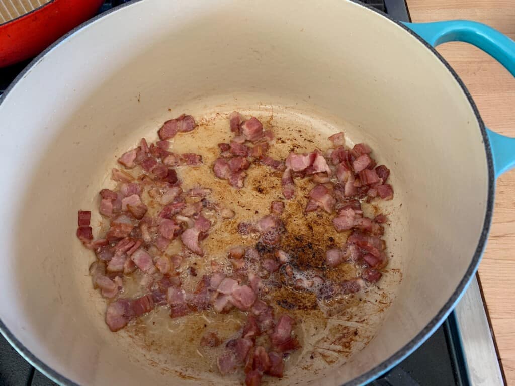 bacon frying in a blue dutch oven