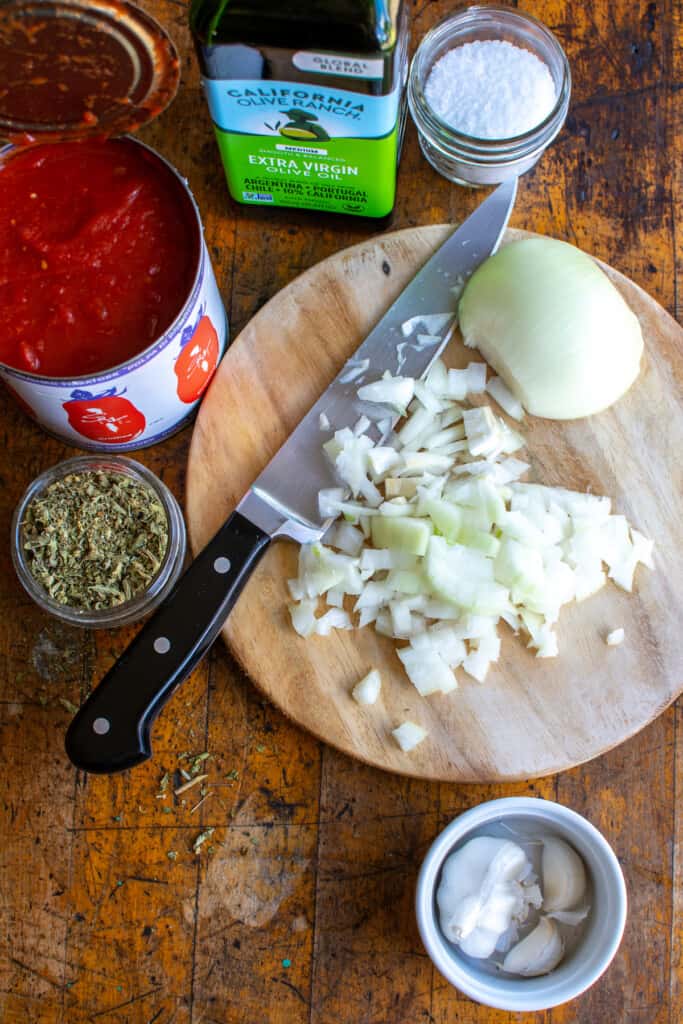 All the ingredients needed to make marinara sauce including canned tomatoes, onion, garlic, salt, and more. 