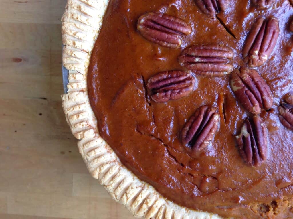 A pie topped with pecan halves sitting on a wood table. 