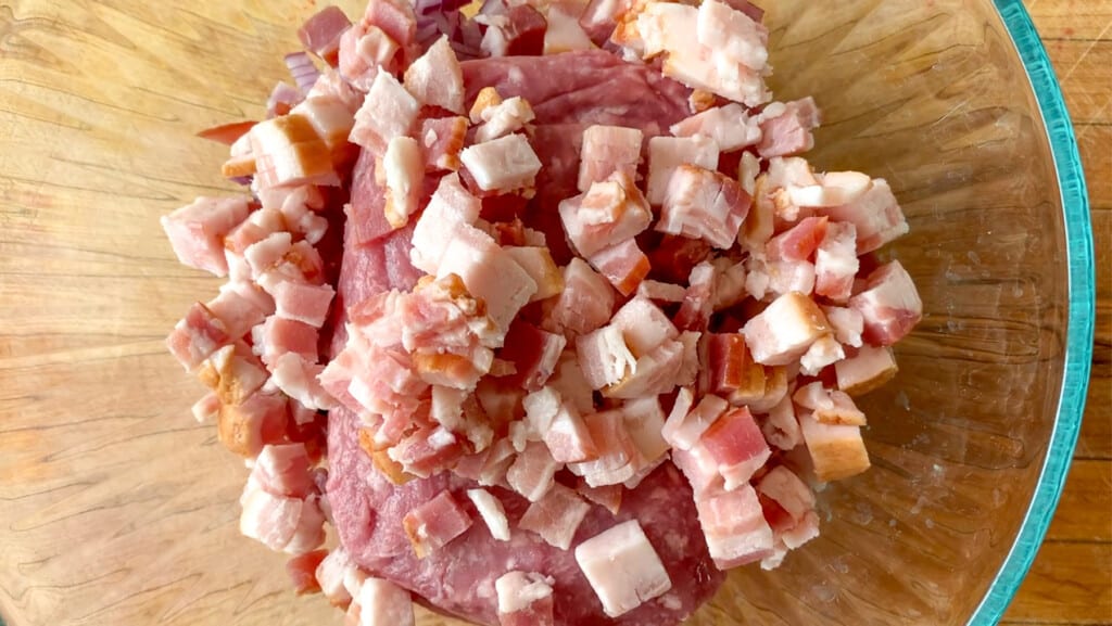 Ground pork and chopped bacon in a glass bowl. 