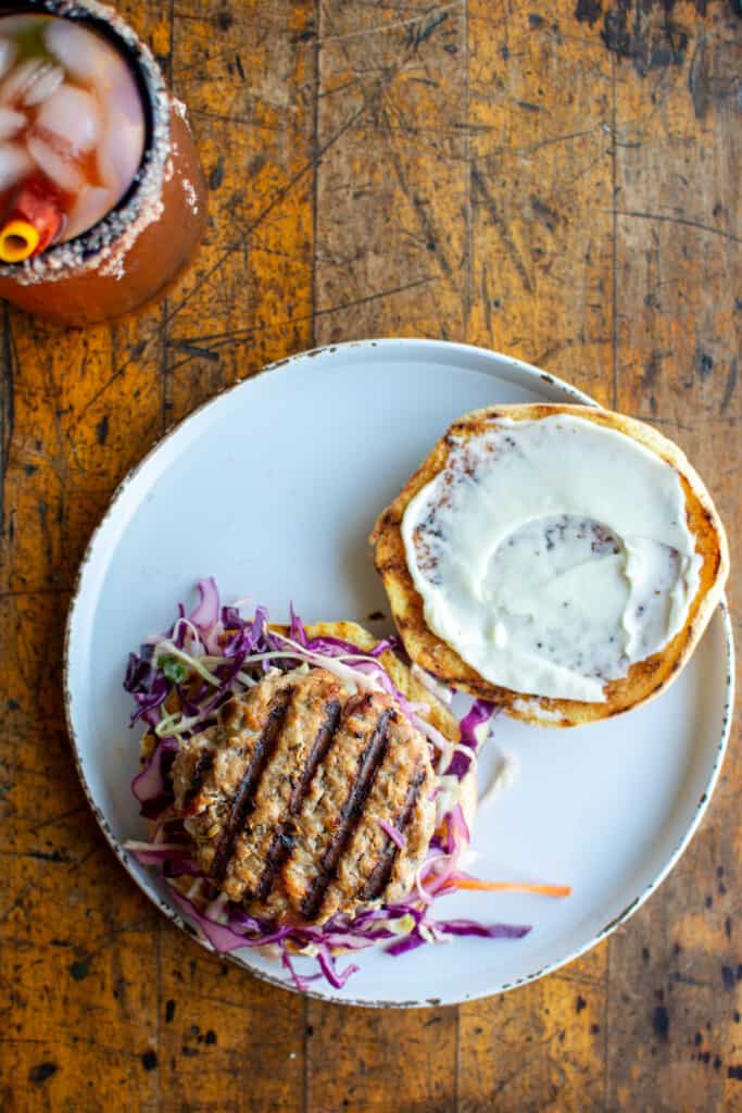 A pork burger on a bun with the top off and the top of the bun coated in mayonnaise. 