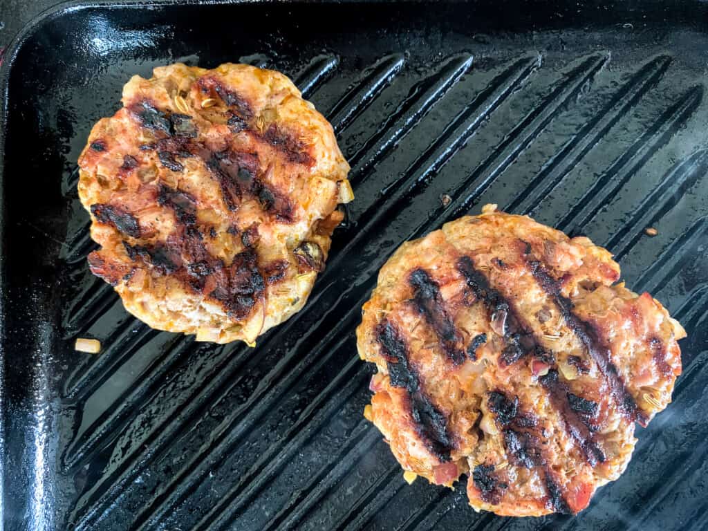 Two ground pork burgers cooking in a grill pan. 