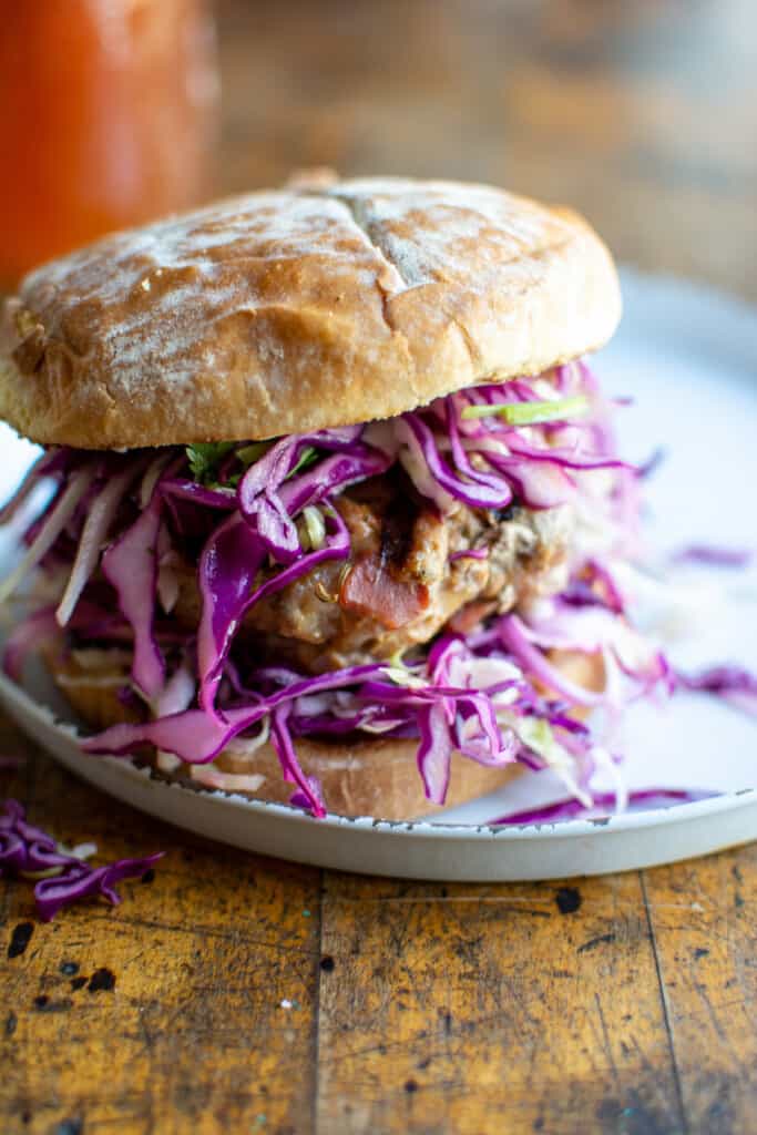A pork burger on a bun topped with lots of red cabbage slaw. 