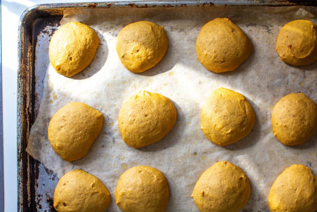 Several pumpkin cookies sitting on a baking sheet that is covered in parchment paper. The cookies have been baked. 