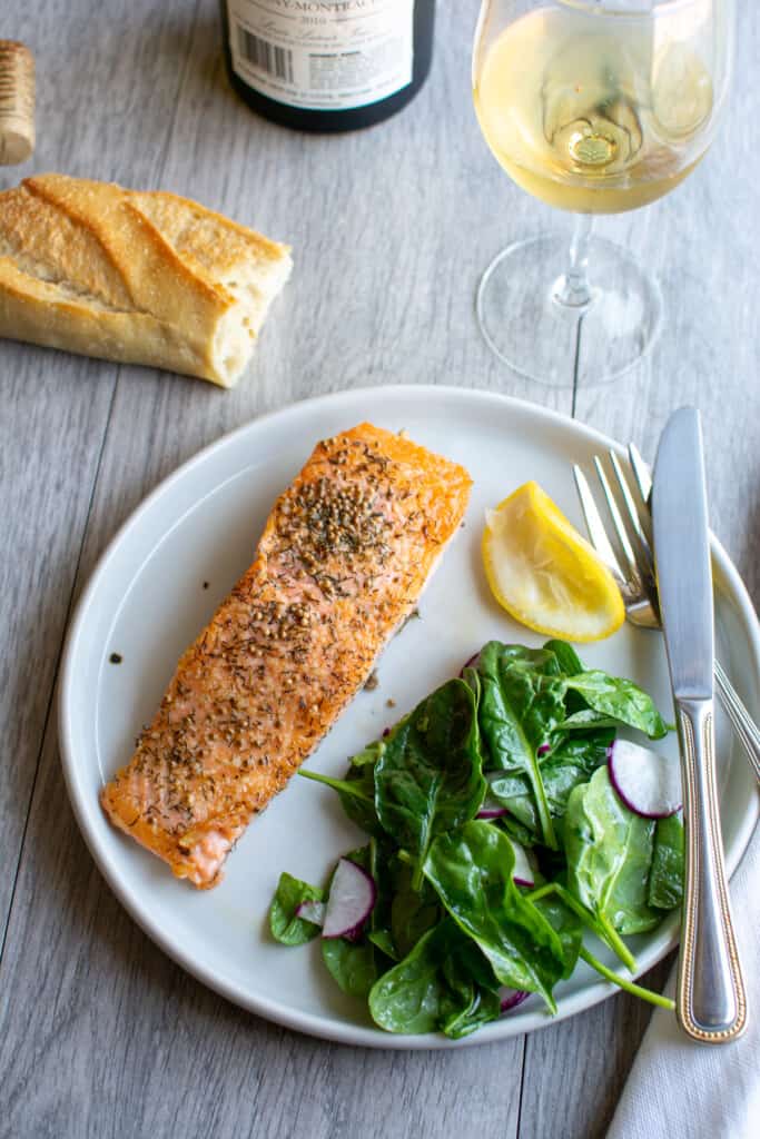 A plate of salmon with a spinach salad next to it and a lemon wedge on the plate. 