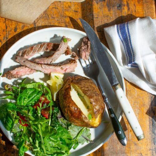 A steak dinner on a plate including a baked potato, steak, and a salad.