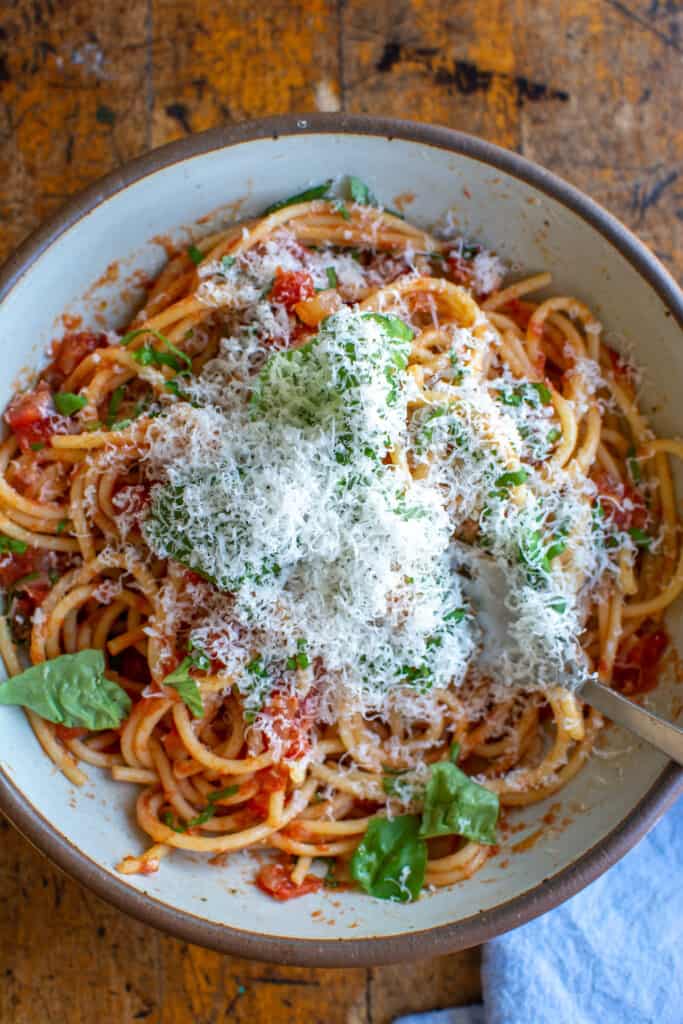 A big bowl of spaghetti with marinara sauce topped with parmesan cheese and fresh basil with a fork sticking out of the bowl. 
