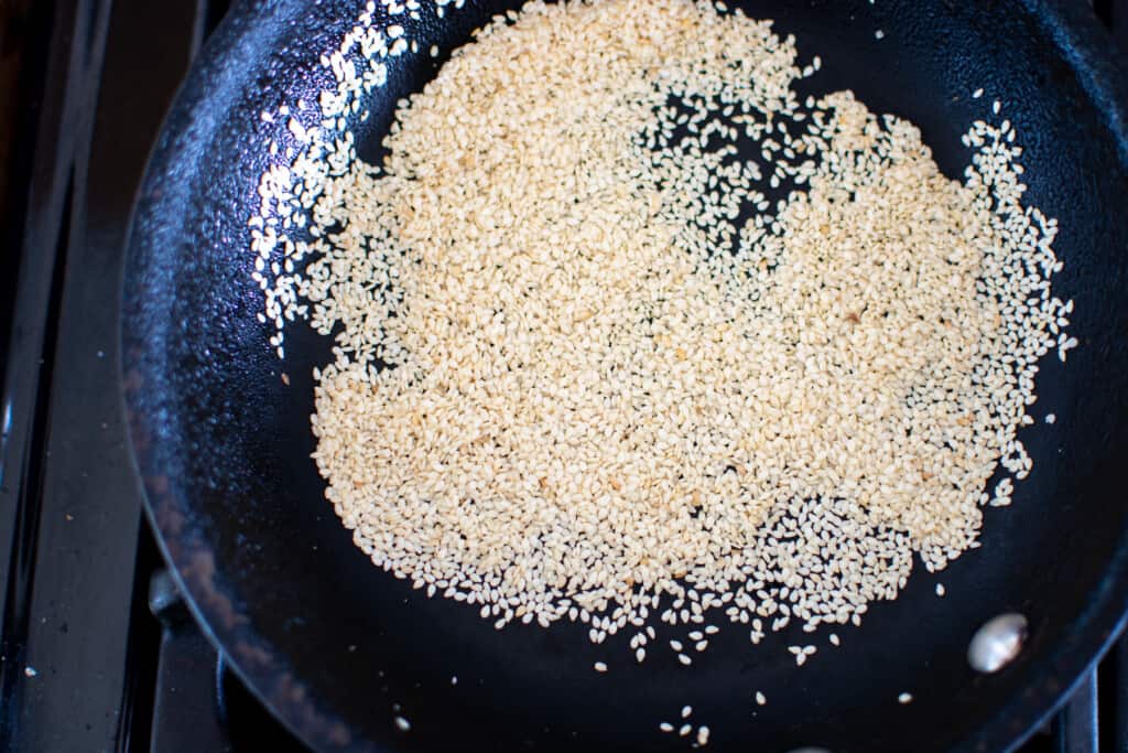 A small black frying pan filled with sesame seeds being toasted on the stove top. 