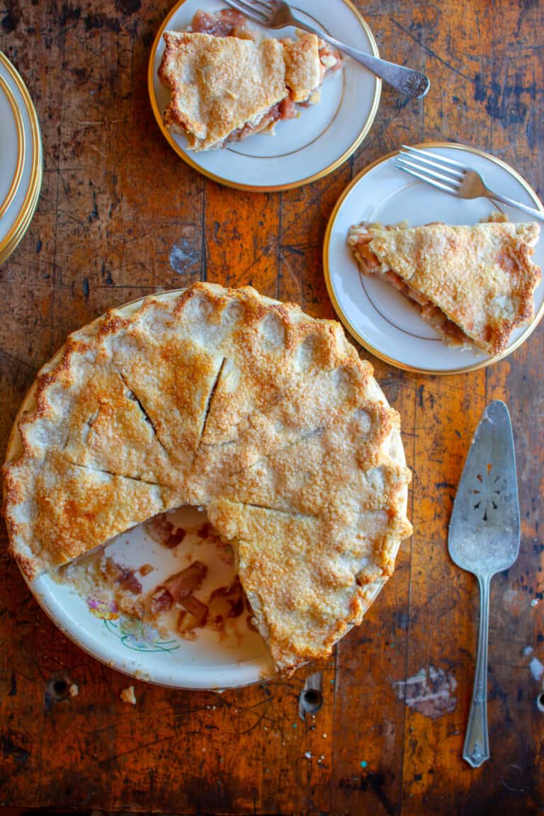 A apple pie with two pieces cut out and the two pieces are sitting on plates behind the pie