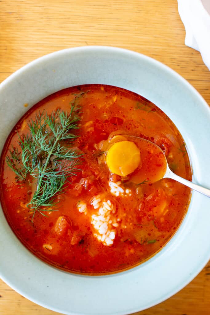 A green bowl filled with tomato soup with dill with a sprig of dill on top and a spoon dipping into the bowl. 