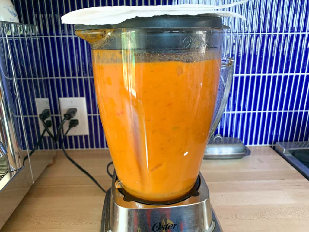 A blender on the counter filled with hot soup being blended. 