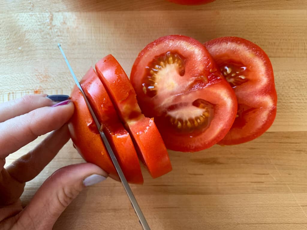 A hand chopping a tomato on a cutting board. 