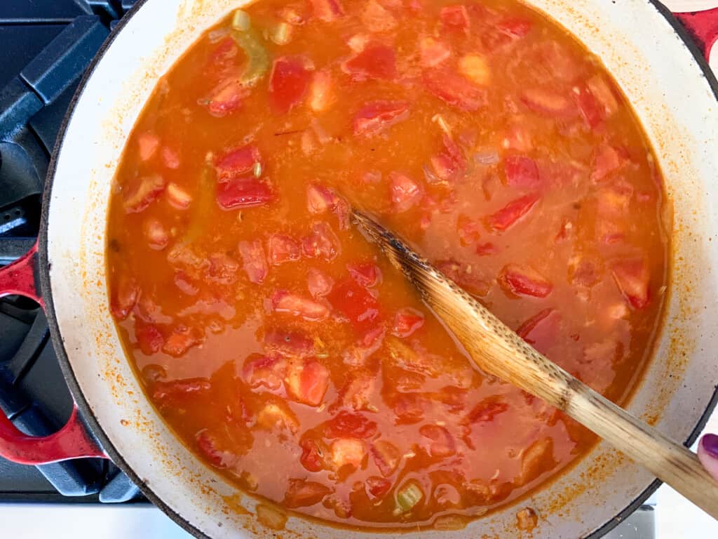 A pot on the stove with soup in it being stirred with a wood spoon. 