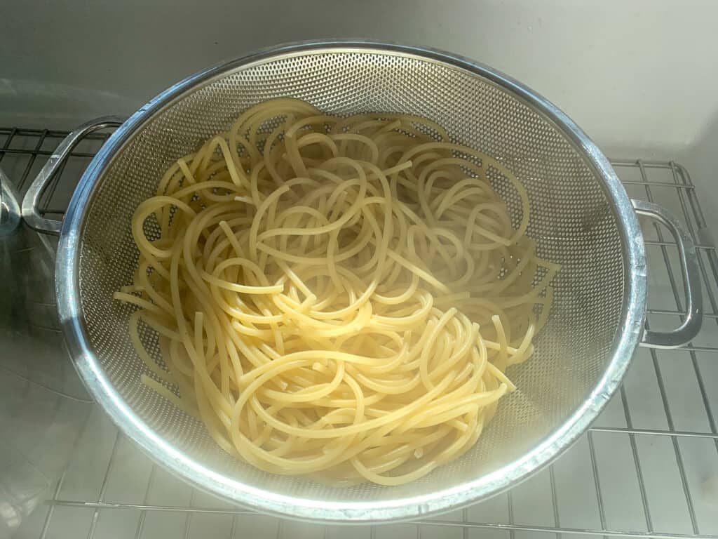 Long pasta noodles sitting in the colander in the sink. 