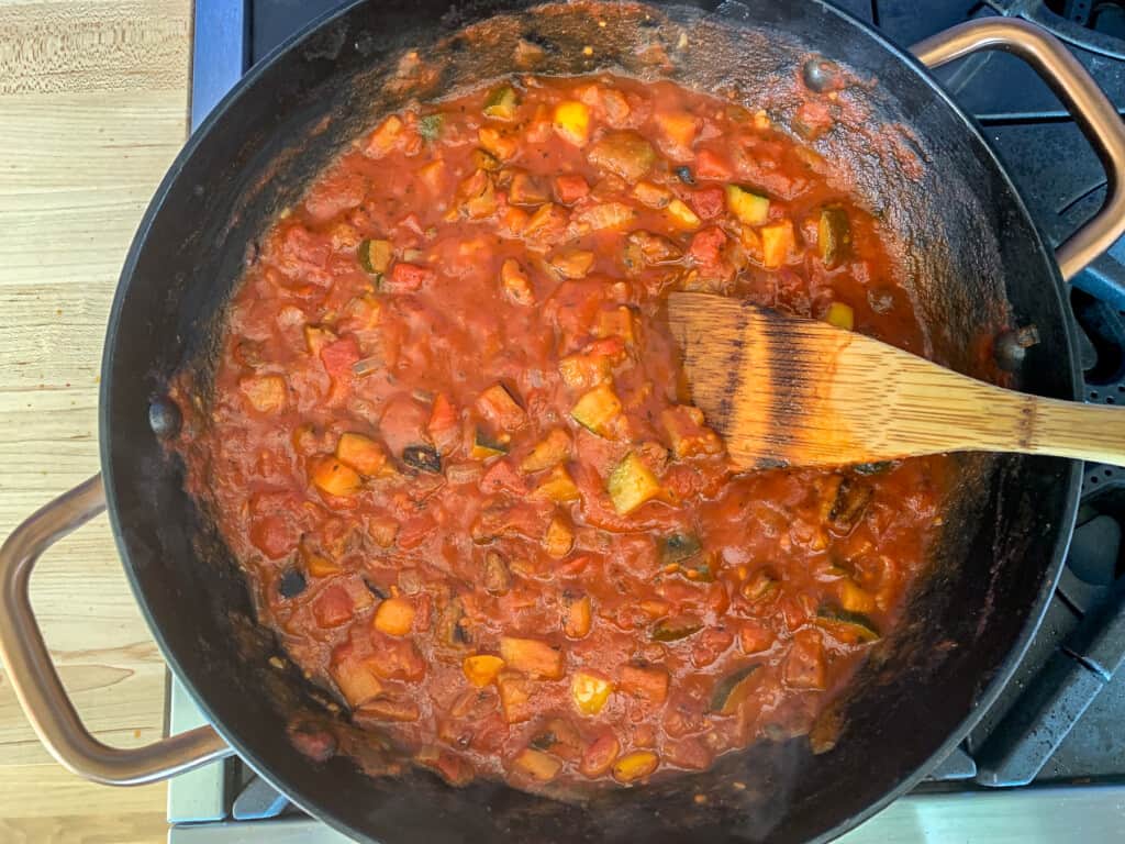 Tomato sauce on the stove with peppers, eggplant, and zucchini in it. 