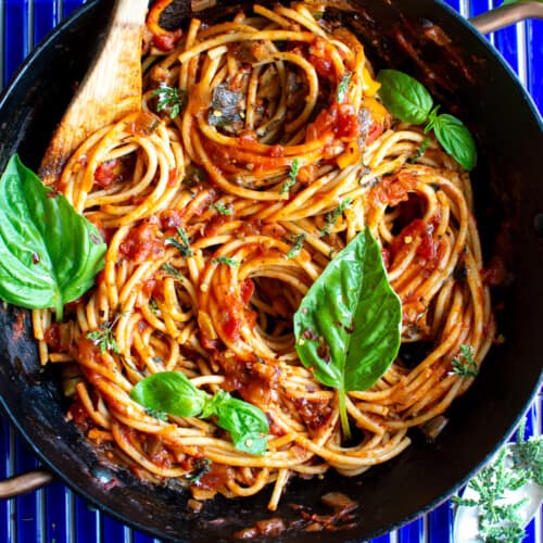 A pot of pasta with vegan bolognese sauce on a blue background with basil leaves in it.