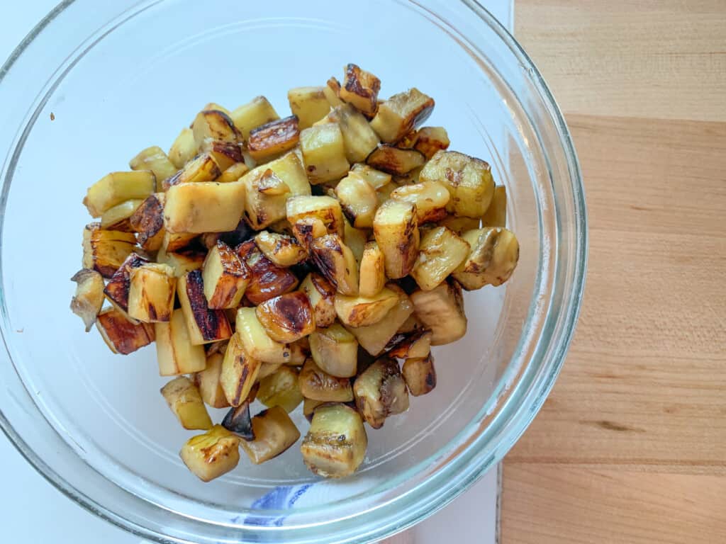 Cubes of eggplant cooked until brown and placed in a glass bowl. 