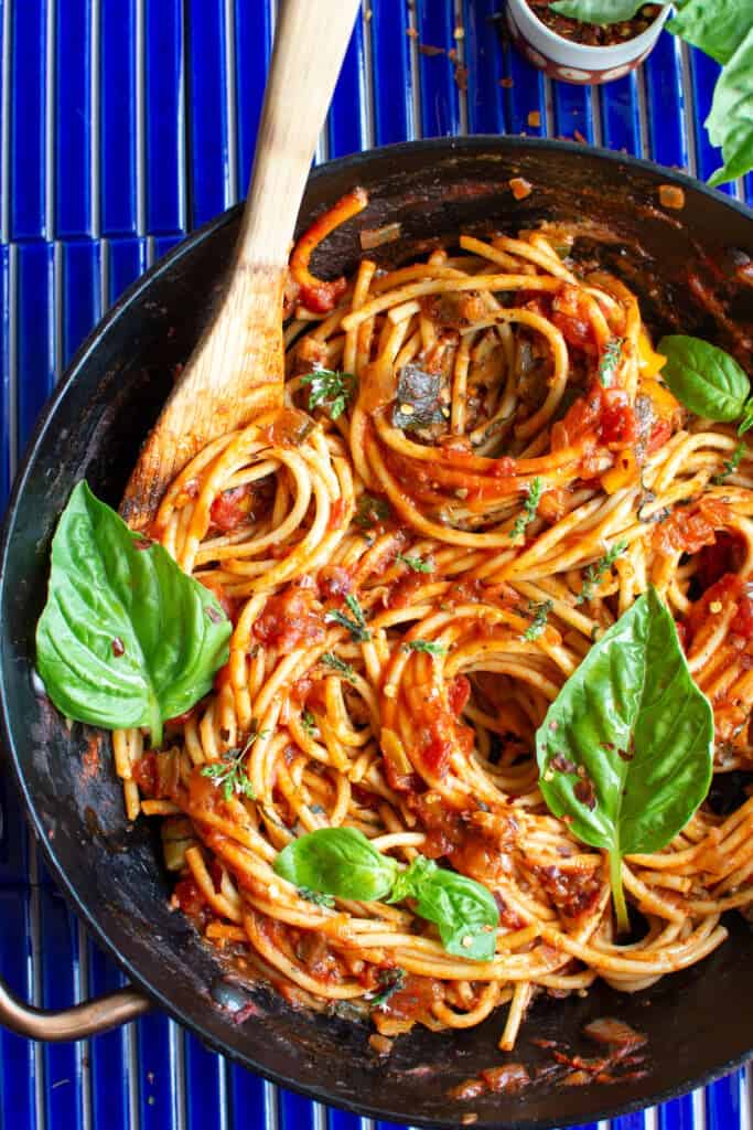 Vegan bolognese with eggplant recipe topped with basil leaves on a blue background. 