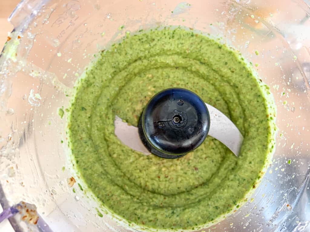 A food processor with basil pesto in the bottom. 