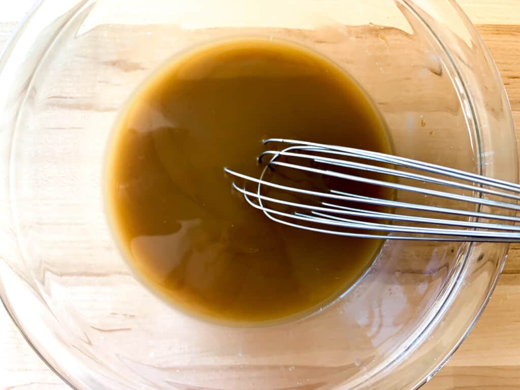 All the sauce ingredients in a glass bowl with a whisk in the bowl. 
