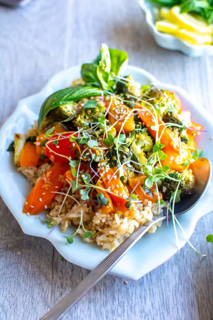 Lemon garlic vegetable stir fry recipe on a white plate with microgreens on top and a spoon next to it with a basil sprig. 