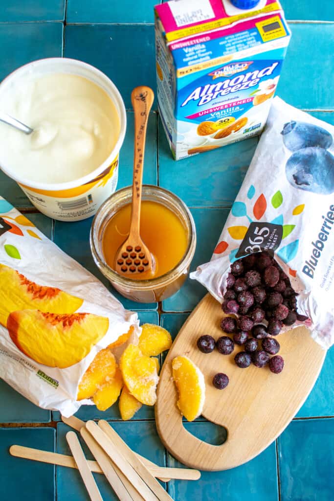 All the ingredients to make yogurt popsicles including yogurt and fruit. 