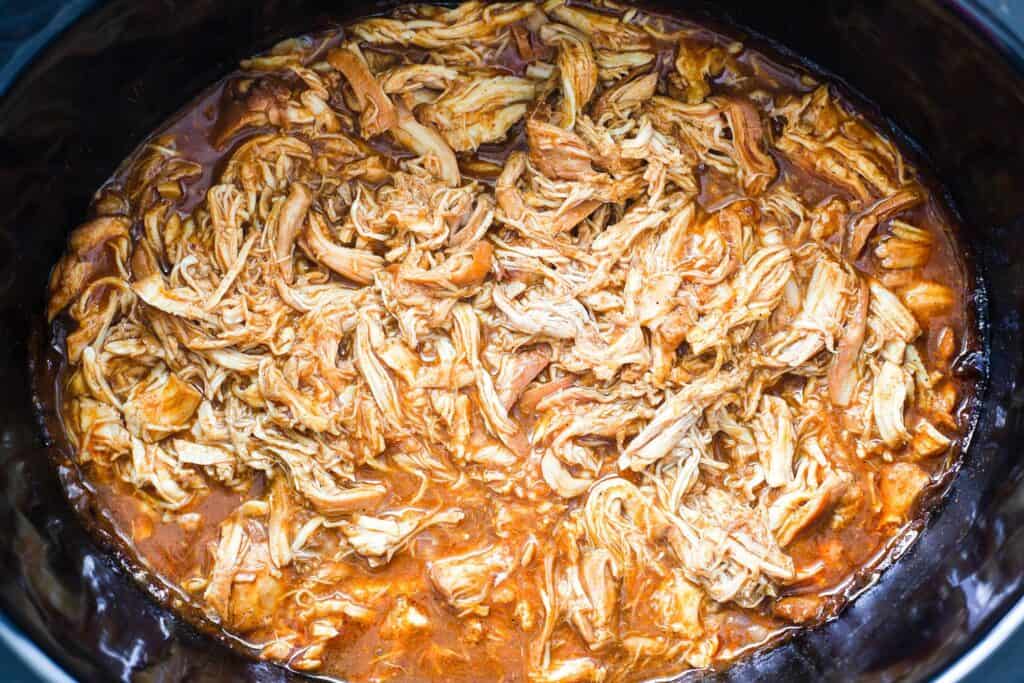 A black crock pot filled with shredded chicken. 