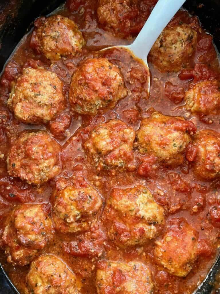 A black crock pot filled with tomato sauce and meatballs with a white spoon sticking out of the pot. 