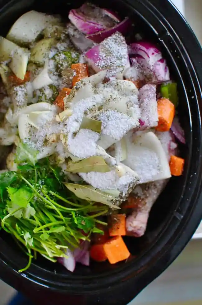 A black crock pot filled with vegetables, herbs, chicken, and salt. 