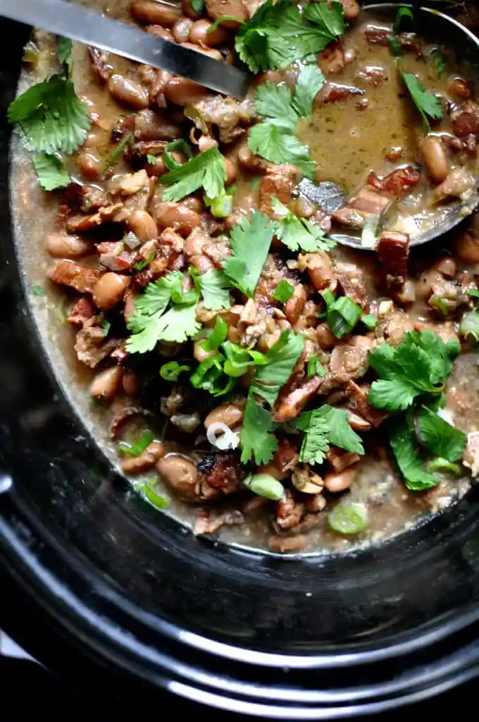 A black crockpot filled with borracho beans and topped with cilantro leaves with a ladle in the pot. 